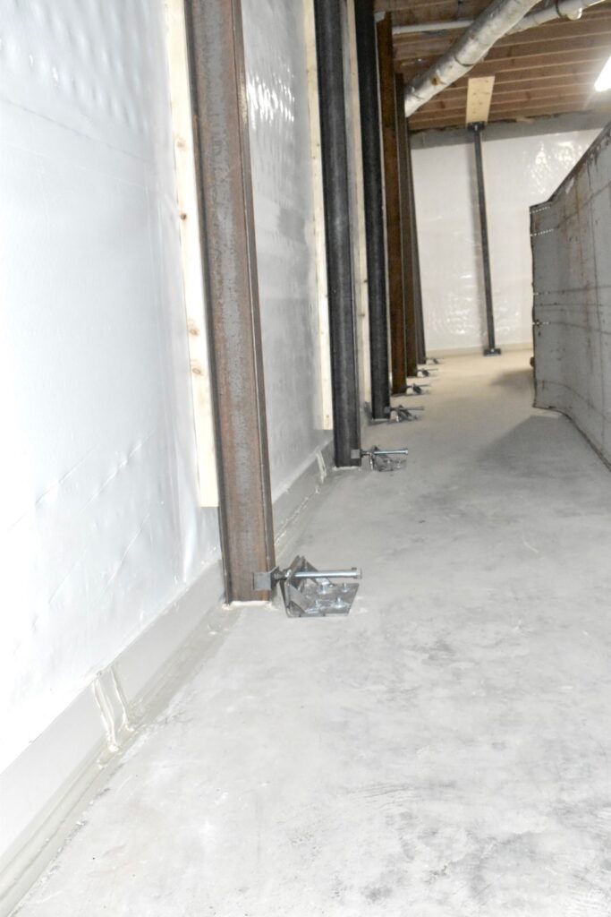 Steel I-beam wall braces installed along a lined basement wall, after repair